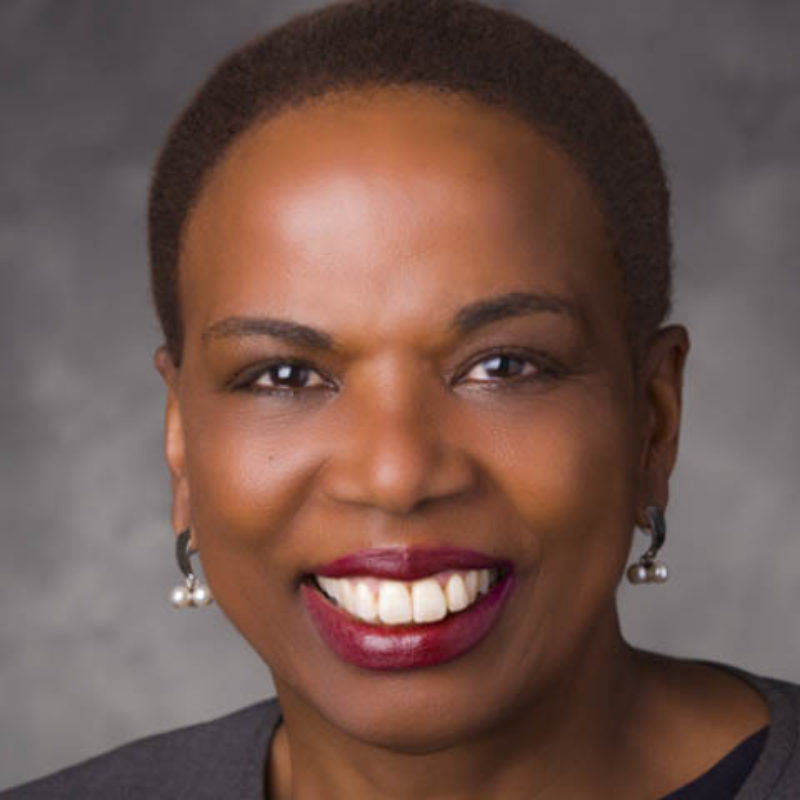 CEO Judy Belk smiles directly at camera in front of a dark grey background