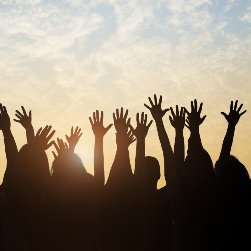 Group of people raising their hands against a sunset