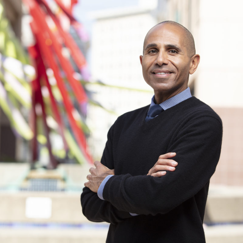 Man with crossed arms smiles at camera, with sculpture in the background