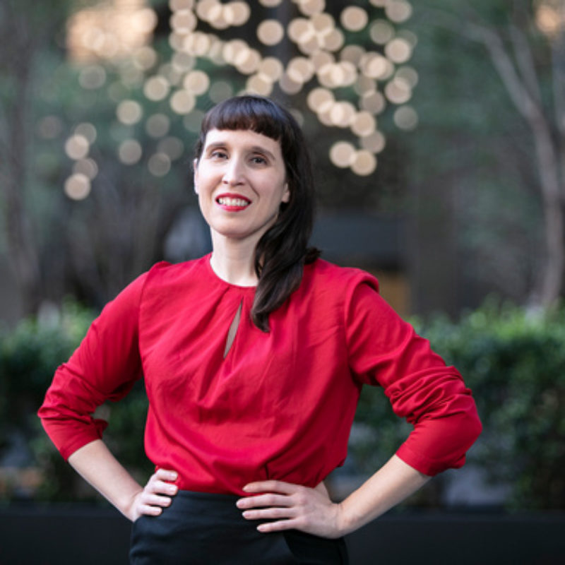 Woman stands and smiles at camera in outdoor setting